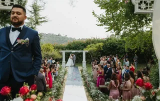 Noivo em primeiro plano e cerimónia de casamento num jardim do Cerrado das Fontainhas, sem cabos no enquadramento.