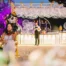 Mulher grávida em vestido branco com coroa segurando bolhas numa festa decorada com balões dourados e pretos à noite.