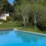 Piscina azul turquesa rodeada de relva verde, palmeiras e vegetação exuberante numa propriedade de luxo.